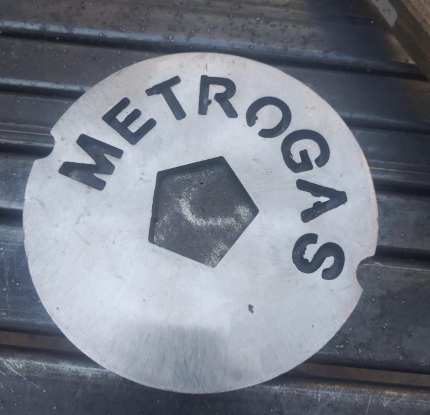 Pieza metálica circular con nombre Metrogas
